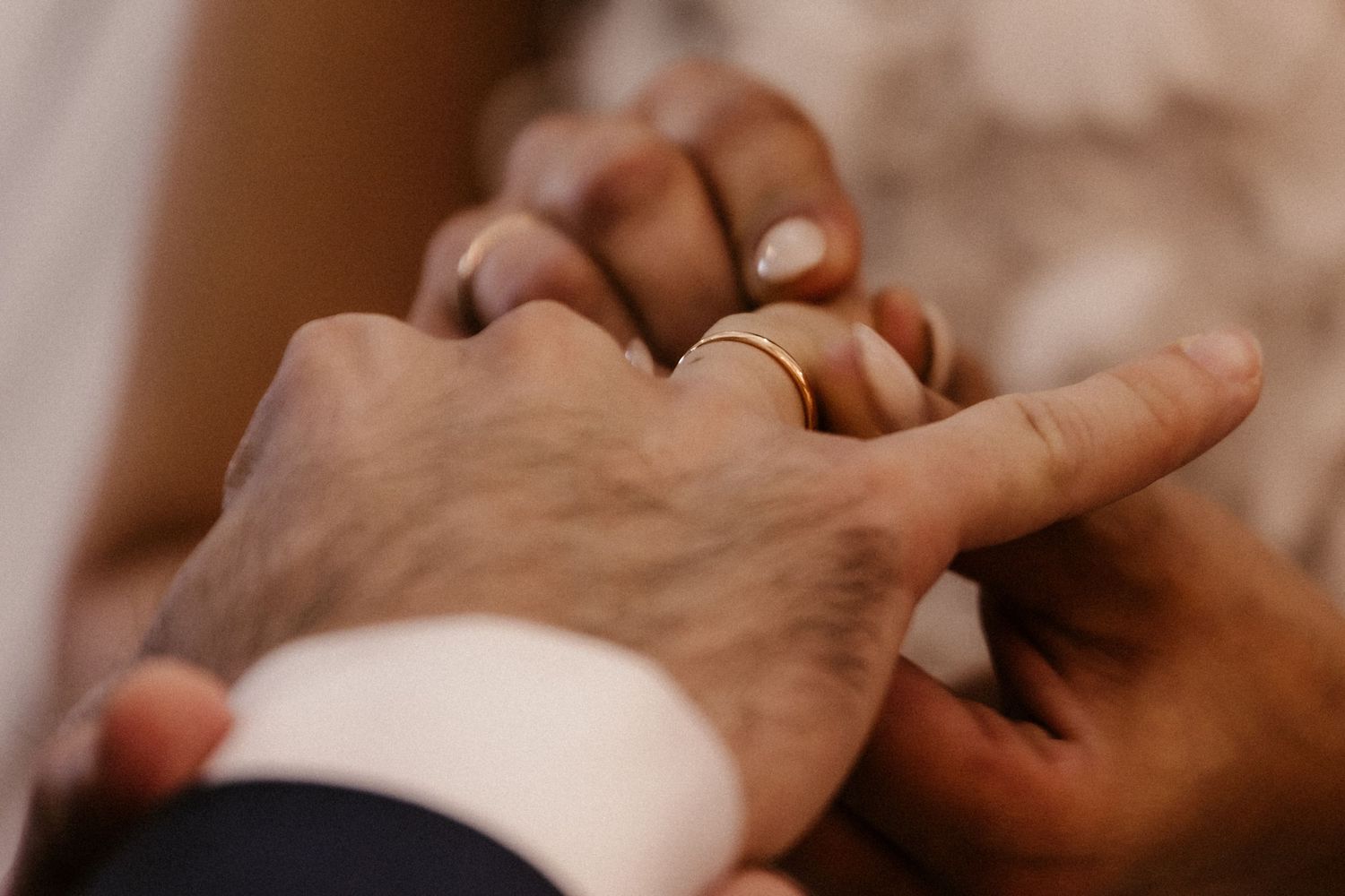 Close-up view of hands holding each other in a gentle, intimate gesture against a warm-toned background.