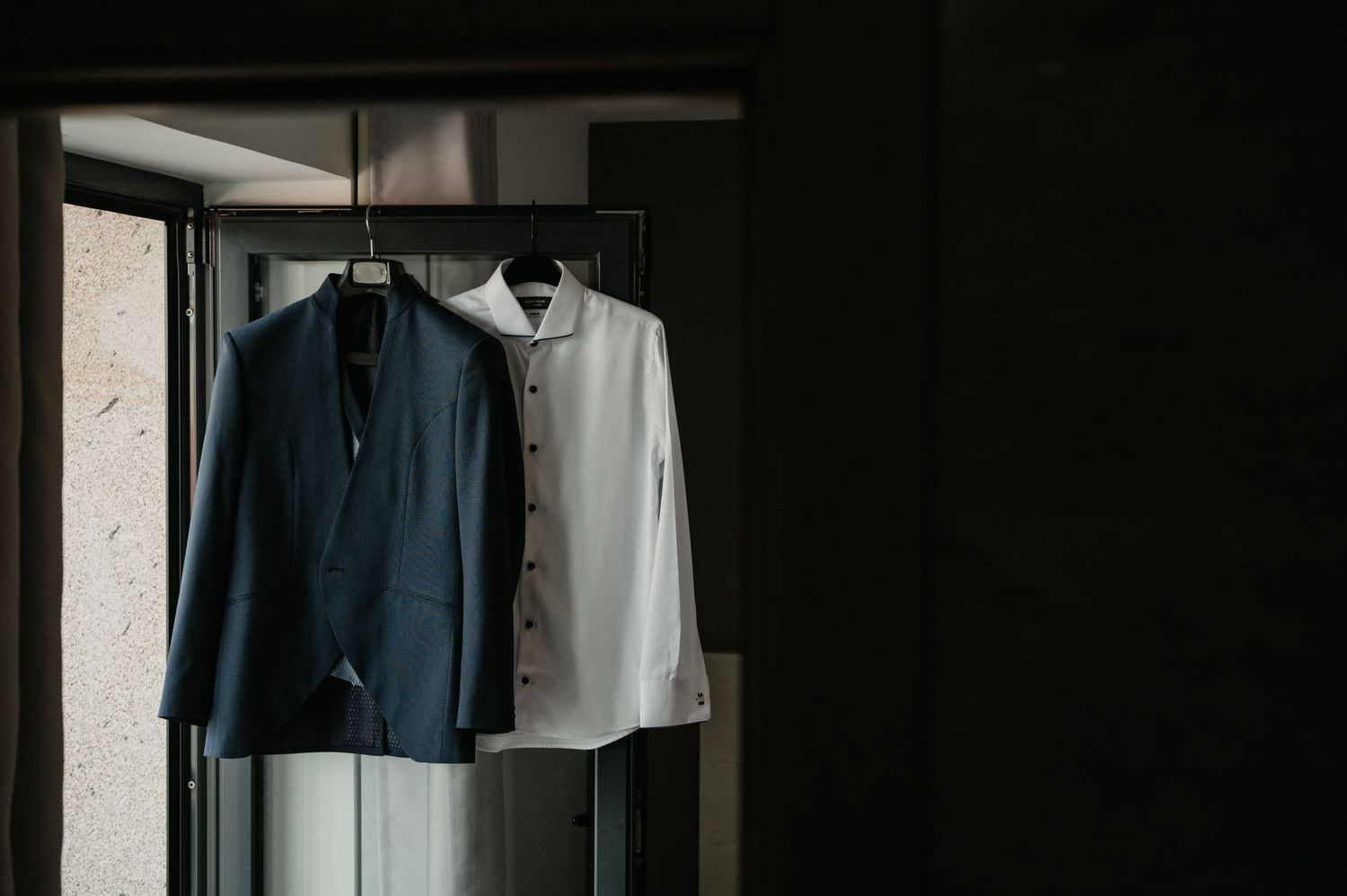 A row of dark suits and dress shirts hanging neatly on wooden hangers in a closet.