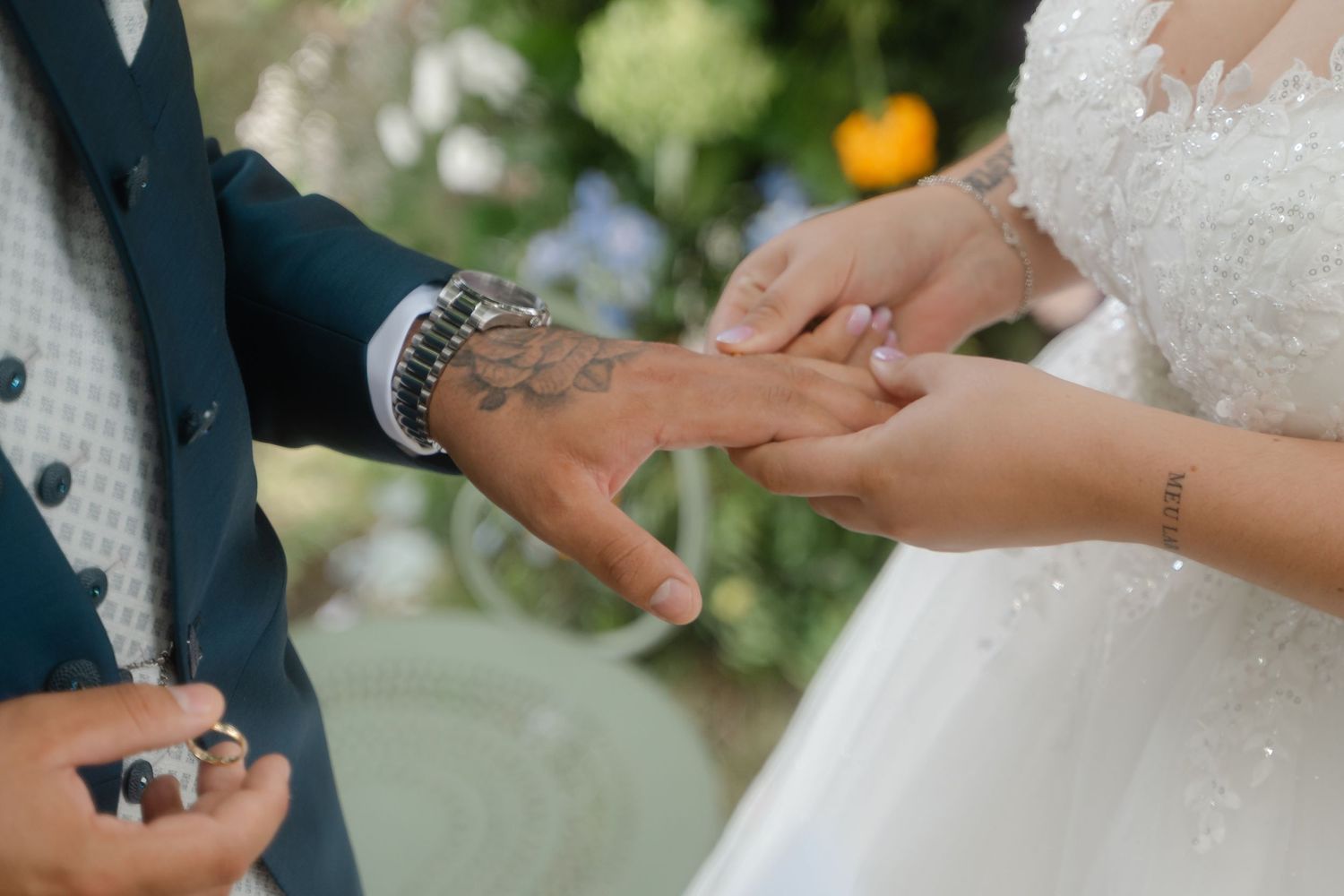 Close-up shot of hands exchanging rings during an elegant wedding ceremony with floral decorations in background.