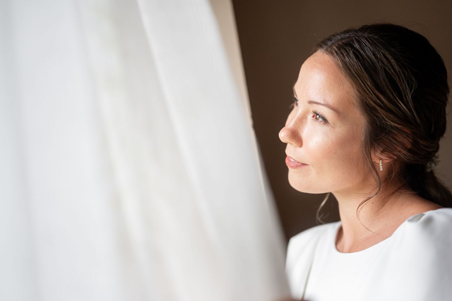 A profile view of a woman in natural light against a white background with her hair pulled back in a bun.