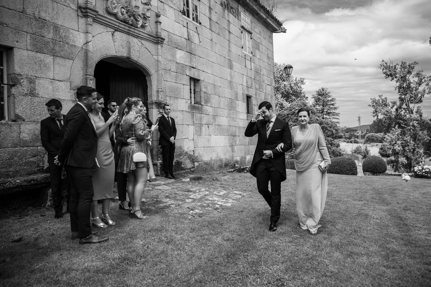 Black and white wedding sequence showing couple walking outside stone building with guests.