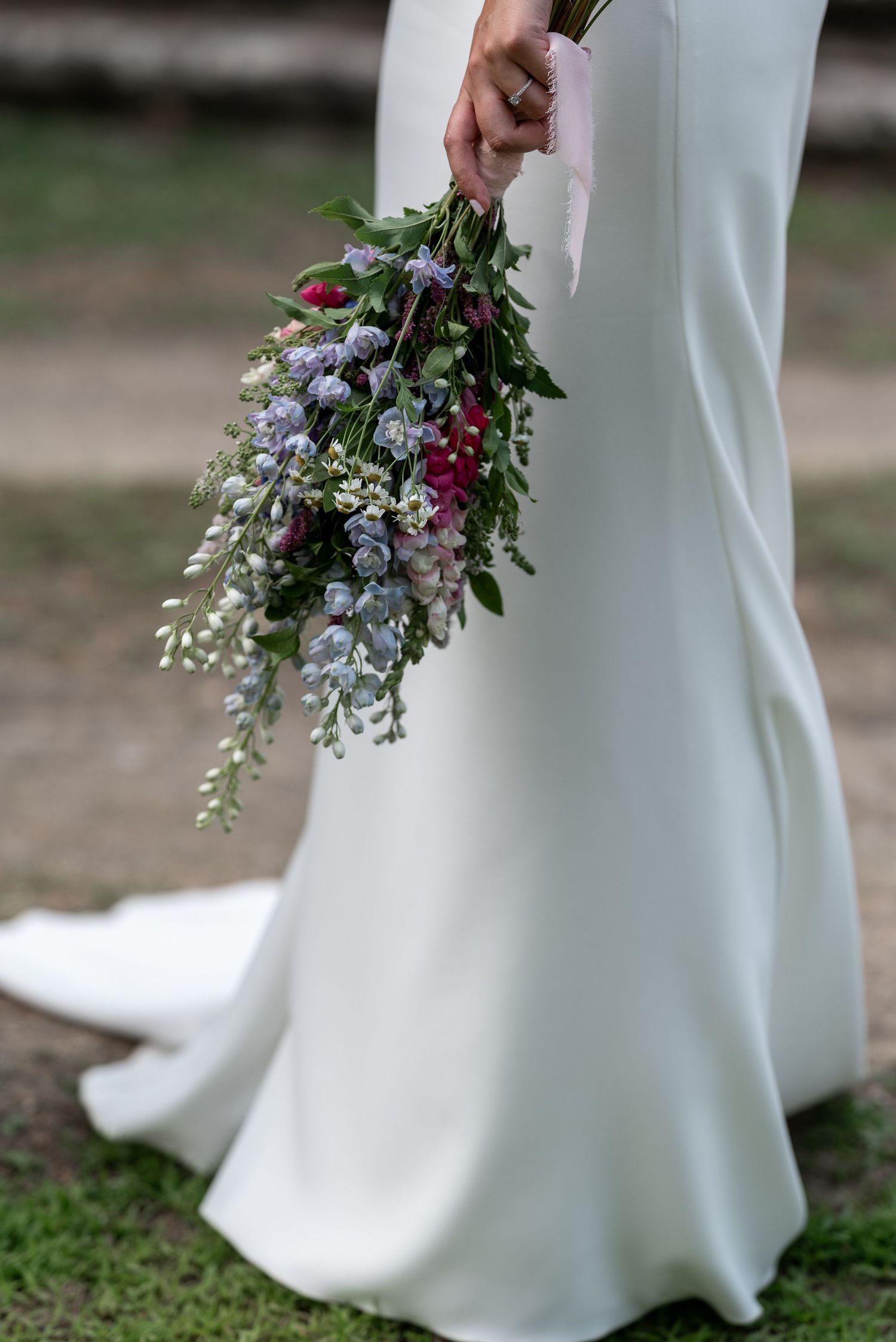 Close-up view of white wedding dress hem with delicate purple and pink floral bouquet details.