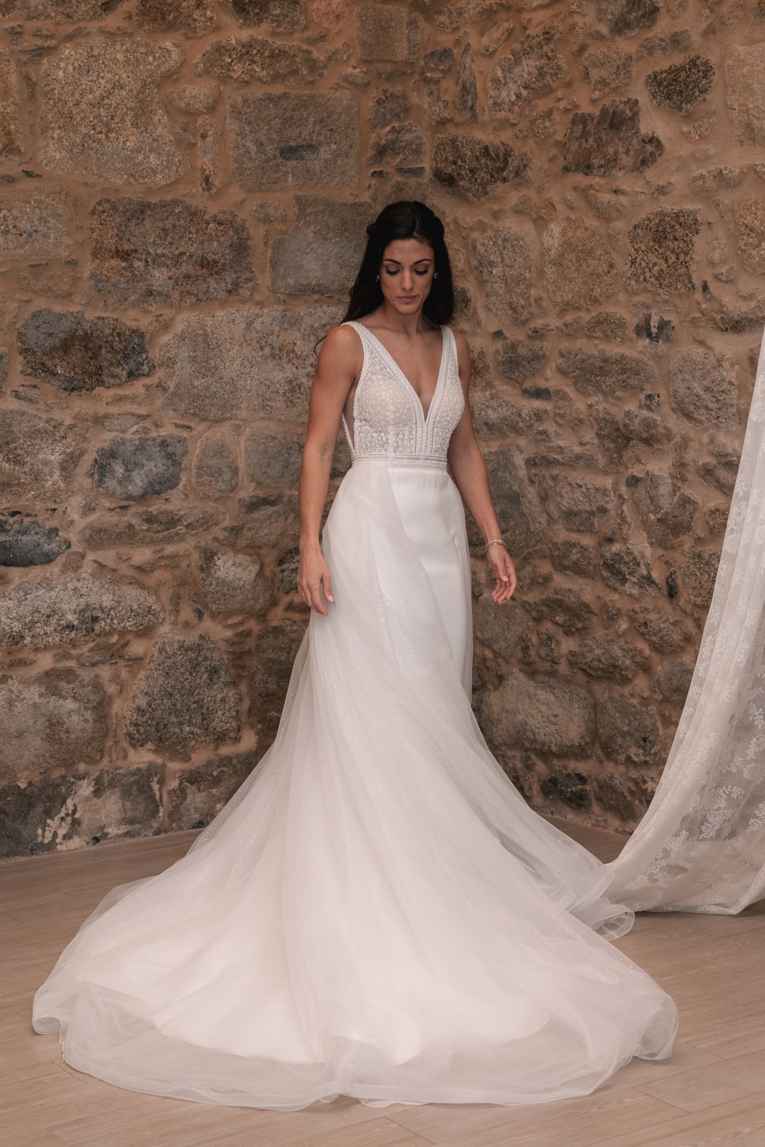 A flowing white wedding dress with sparkly tulle skirt twirls elegantly against a rustic stone wall backdrop.