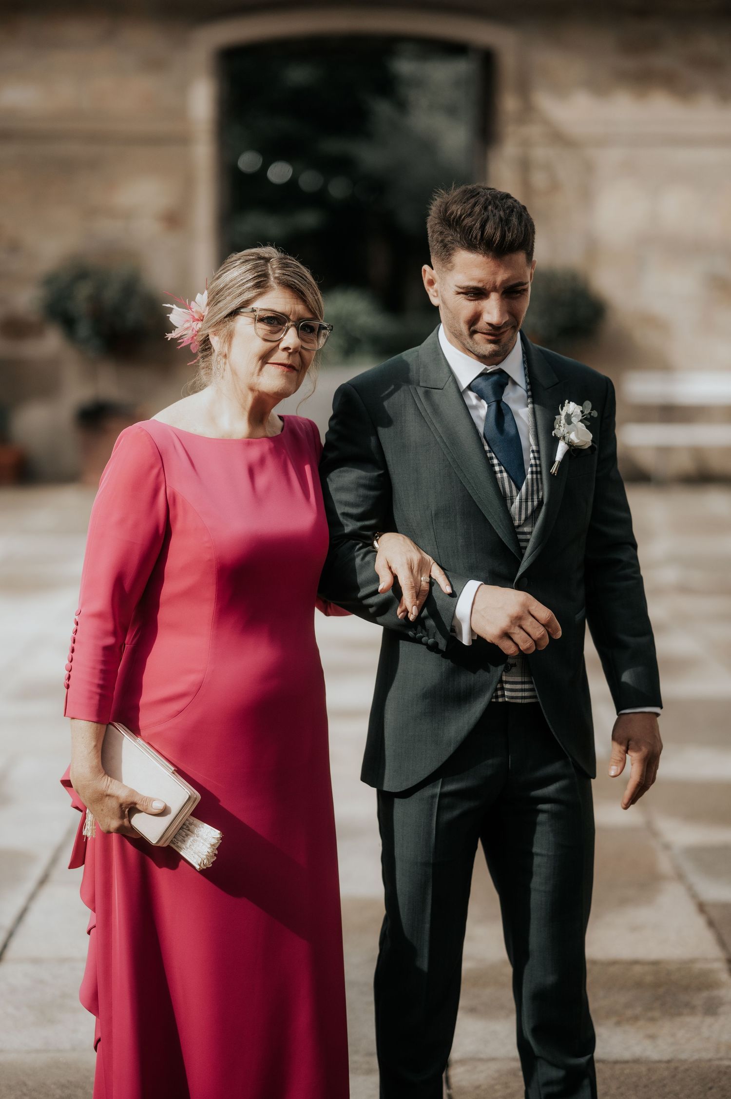 A couple in formal attire, with the woman wearing a vibrant red dress, share candid moments together outdoors.