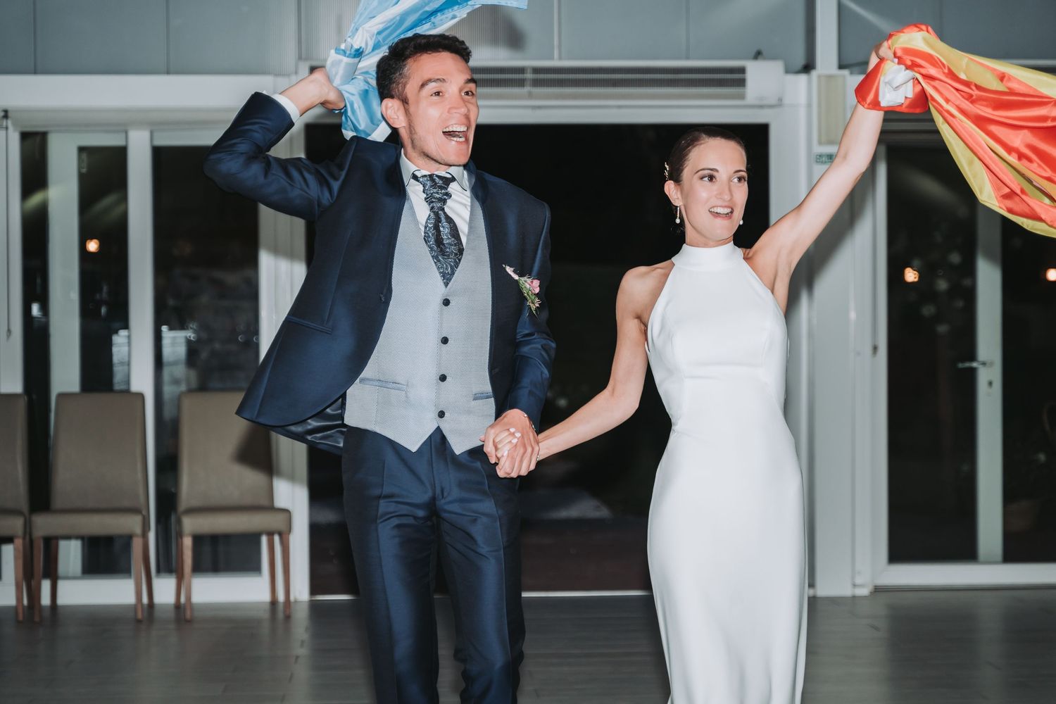 Wedding party celebrates with orange and navy fabric banners while dancing in a modern venue hallway.