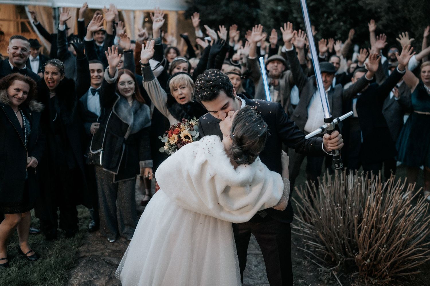 Wedding guests gather outdoors to celebrate the newlyweds during an evening reception.