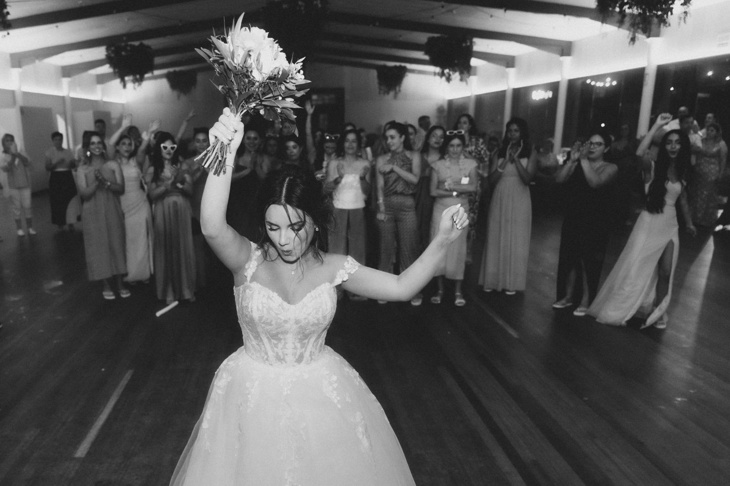 A couple shares their first dance at a wedding reception surrounded by guests on a dark dance floor.