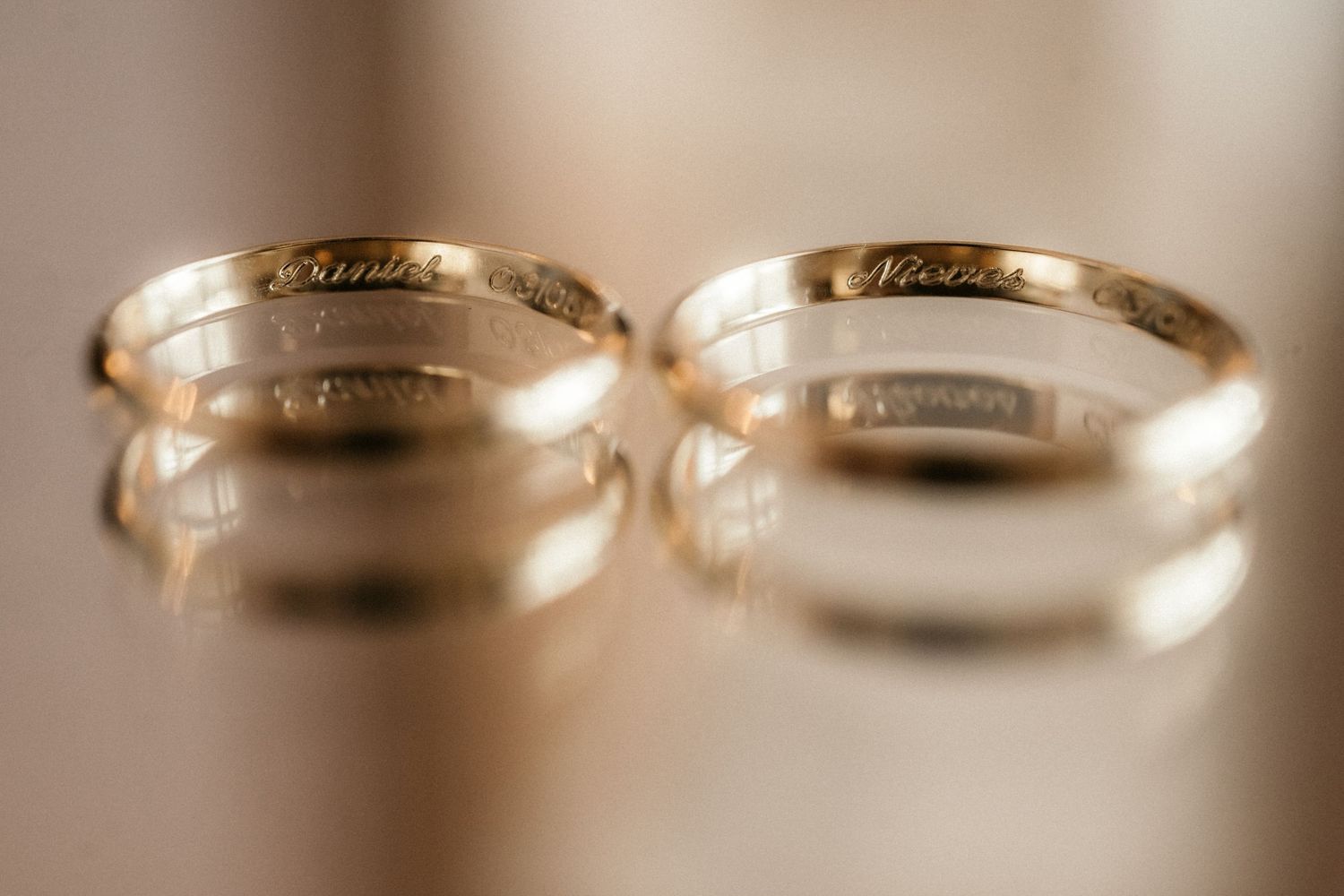 Two gold wedding bands with engraved inscriptions sit side by side in a soft focus close-up shot.