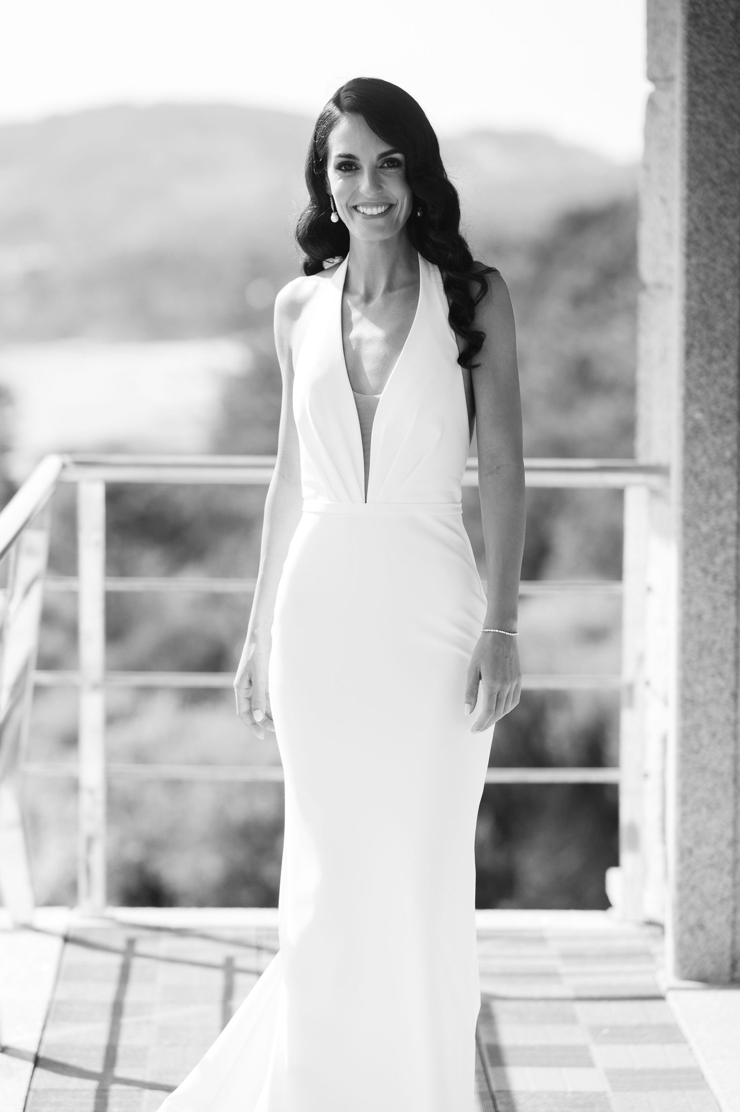 Elegant bride in a sleek white wedding dress poses on a balcony in a series of black and white photos.