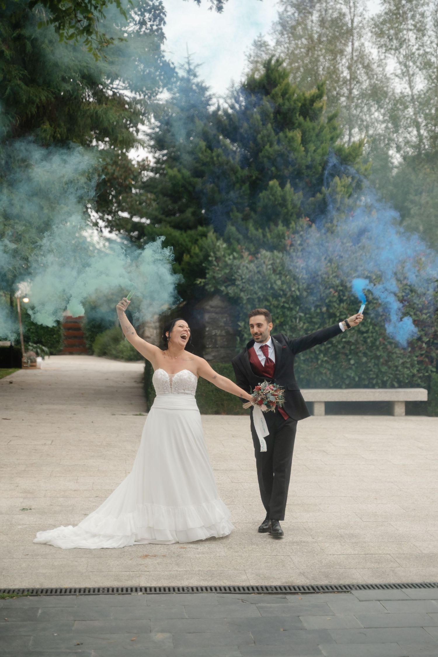 A couple celebrates with colorful smoke bombs on their wedding day, creating a dreamy outdoor photo.