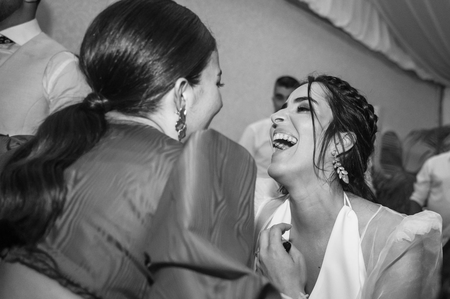 A candid black and white photo captures two people sharing a joyful laughing moment at an event.