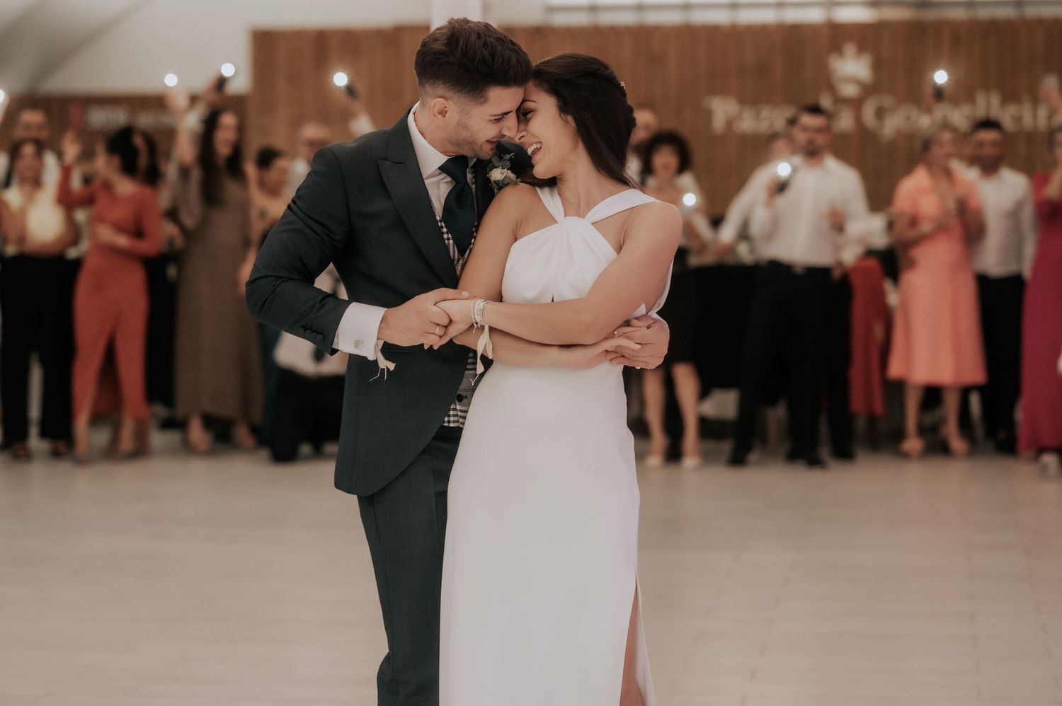 A couple dances together during their wedding reception while guests watch from the background.