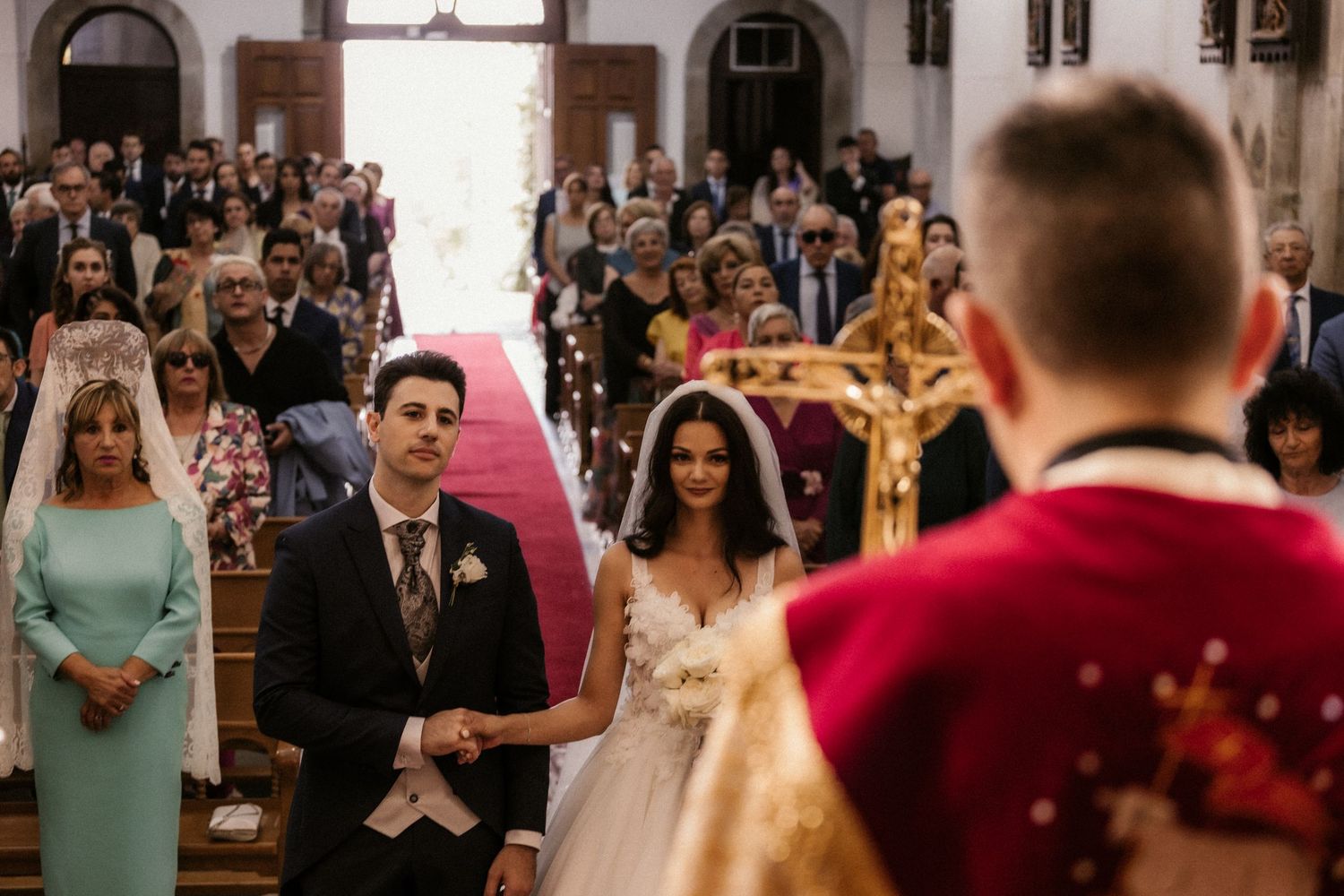 Wedding guests shower newlyweds with flower petals during a joyful ceremony exit at a stone church.