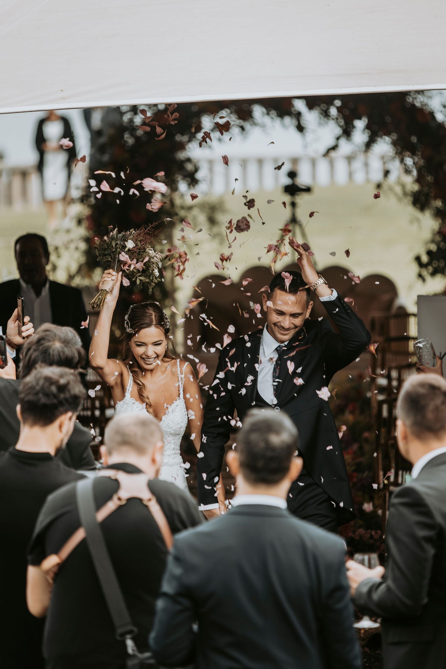 Wedding guests shower the newlyweds with confetti during an outdoor celebration.