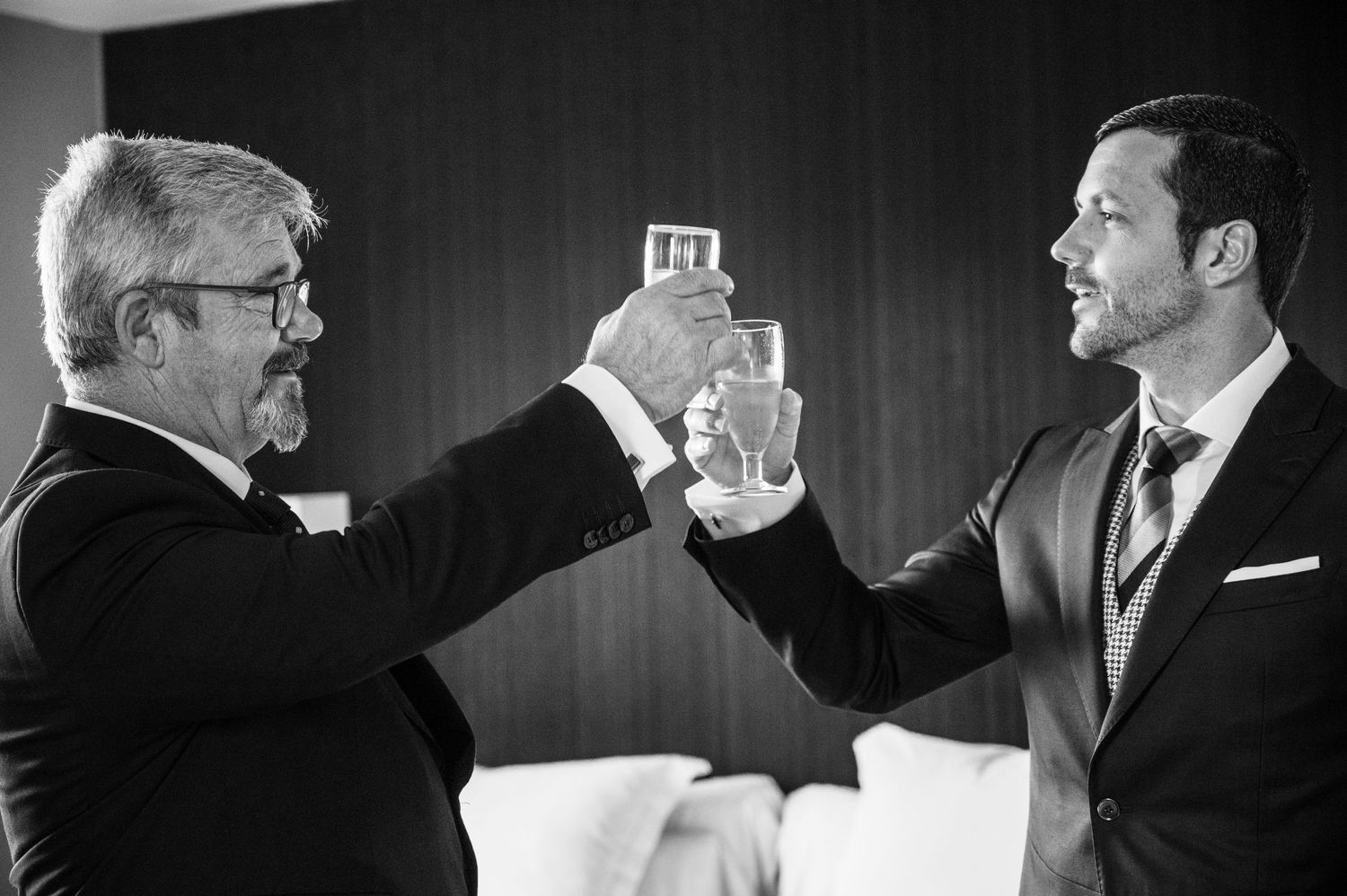 Men in formal suits gather together during what appears to be a wedding preparation moment in black and white.