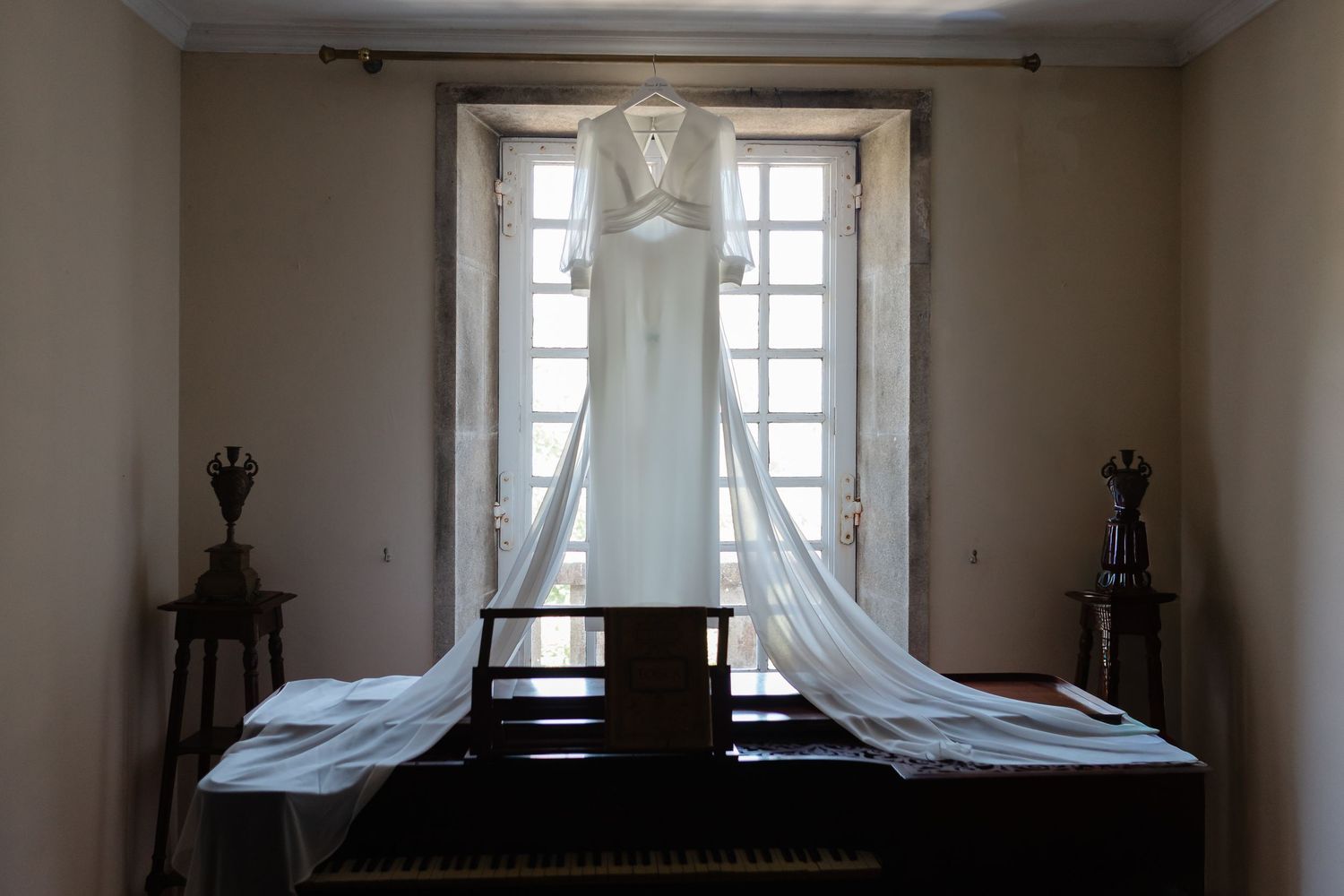A dimly lit bedroom with antique furniture and tall windows with white curtains.