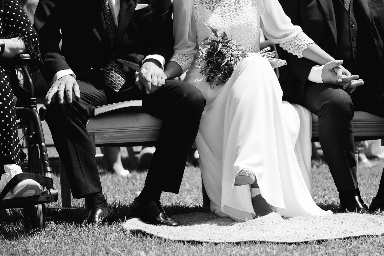 Black and white photograph showing wedding guests sitting on grass during an outdoor ceremony.