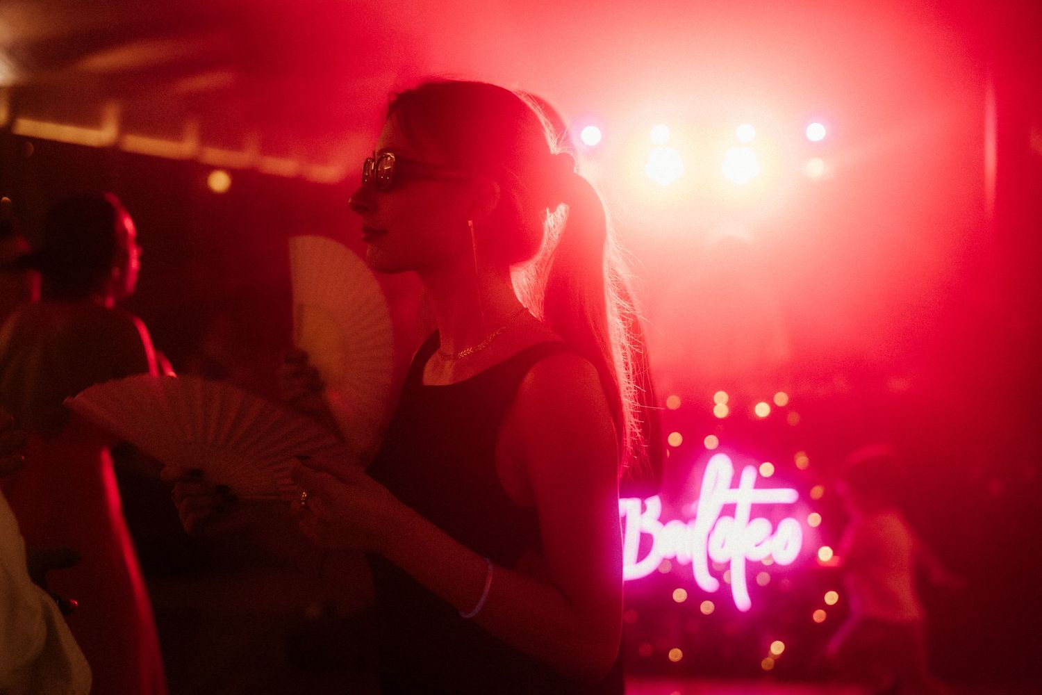 A silhouetted figure dances in front of red stage lighting and a neon sign at a nightclub.