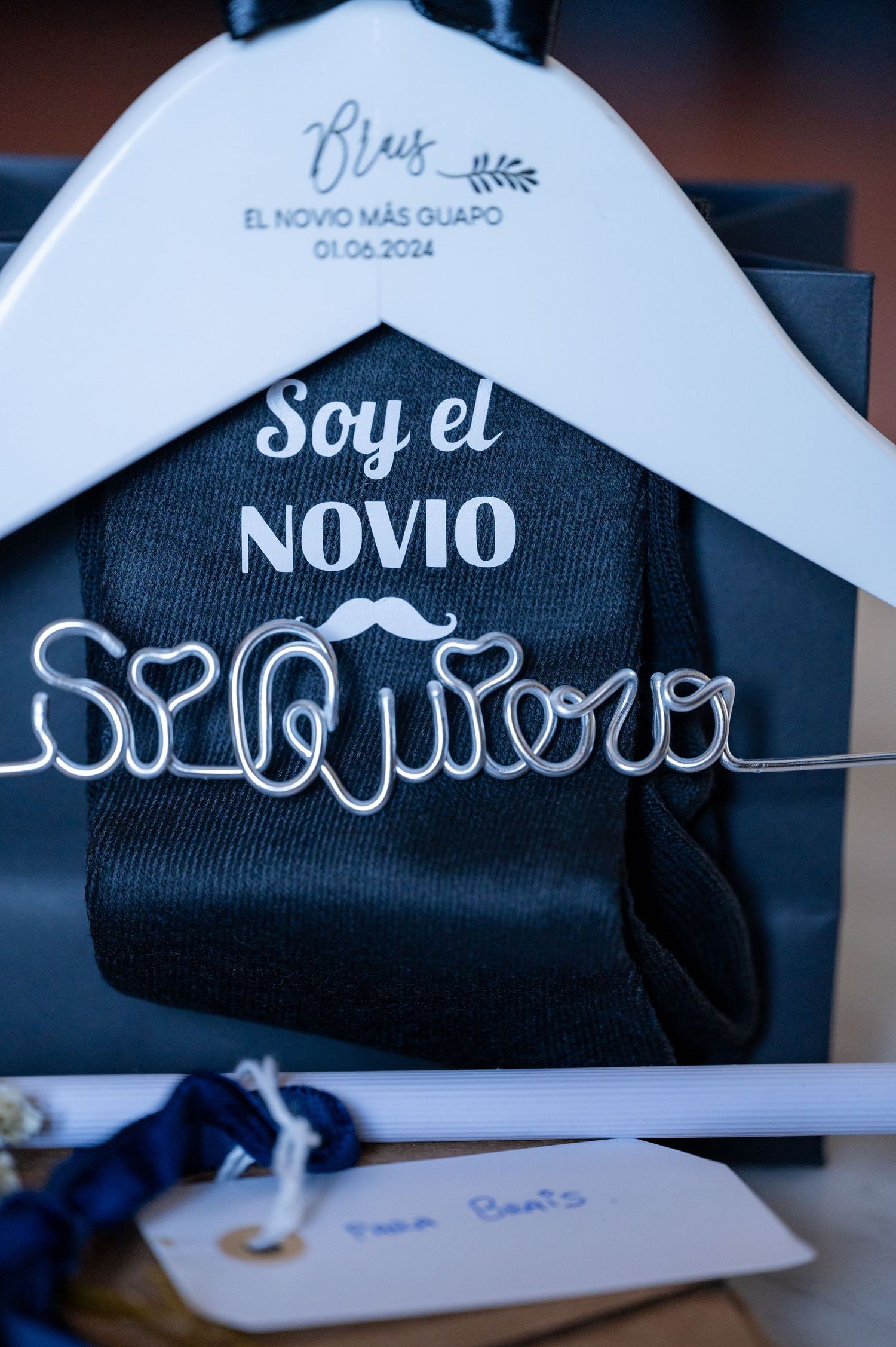 Close-up view of black and white baseball caps with Spanish text 'Novio' and mustache designs displayed on hangers.