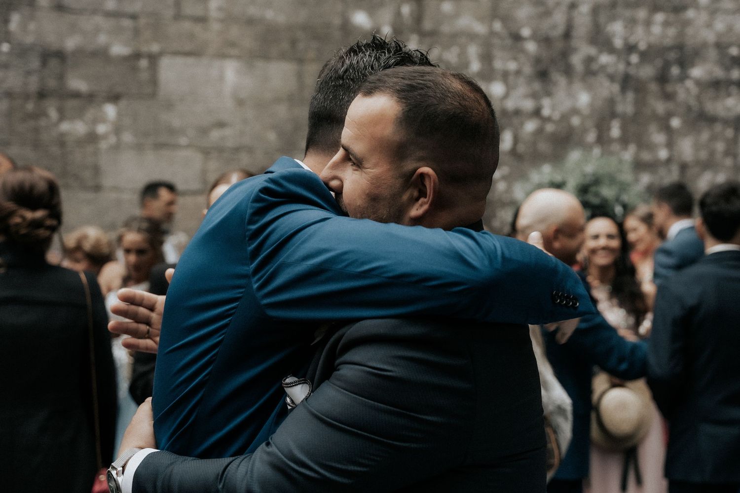A crowd of wedding attendees gather for group hugs and celebrations at an outdoor venue.