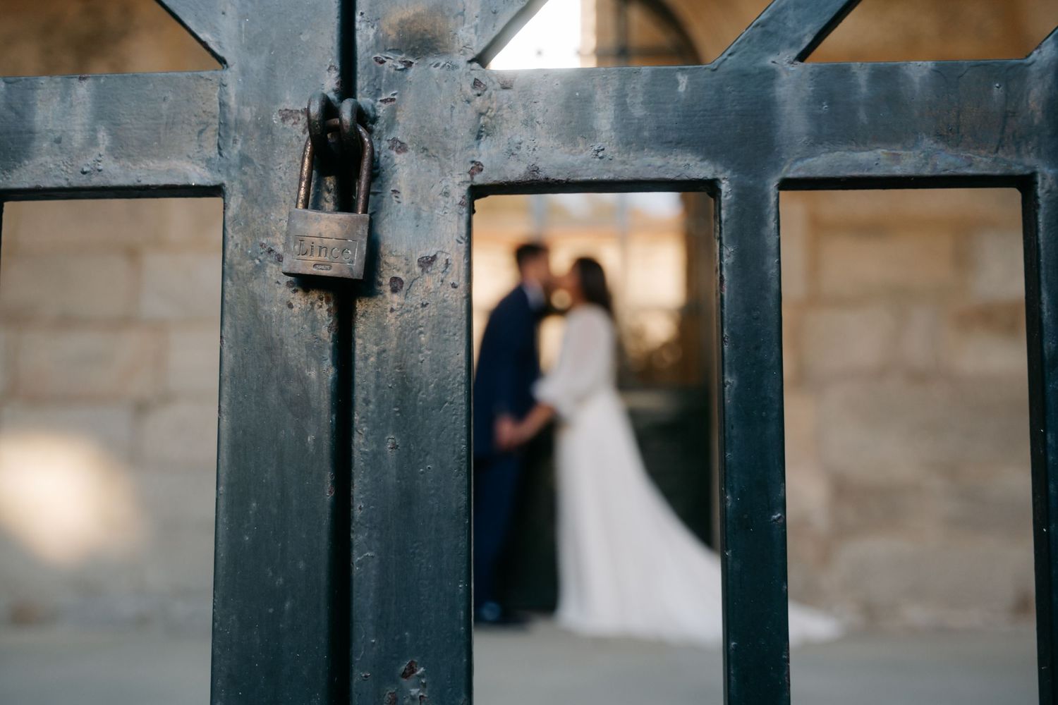 A bride in a white wedding dress stands in front of a rustic stone wall at dusk.