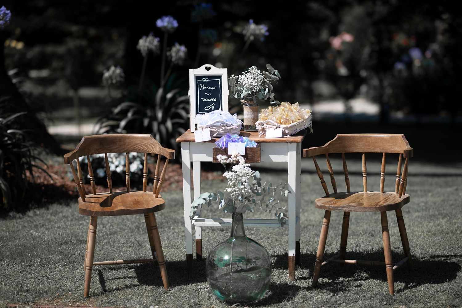 Rustic wooden chairs and tables arranged outdoors with delicate floral decorations create an elegant garden party setting.