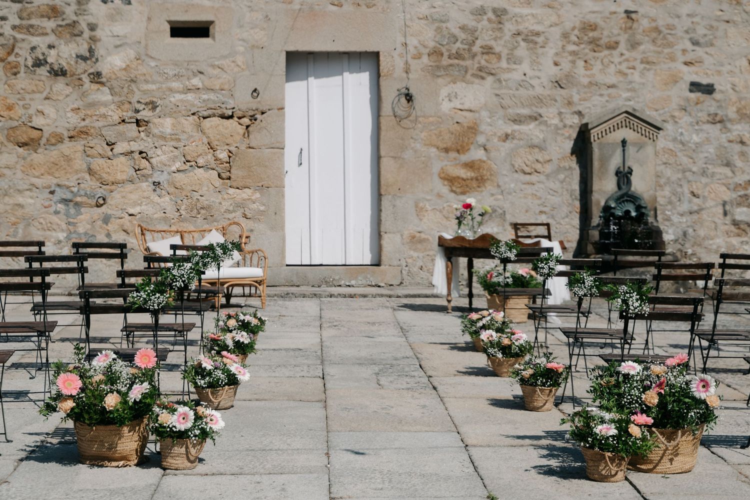 Rustic stone wall exterior with potted pink flowers and white shutters creating a charming Mediterranean ambiance.