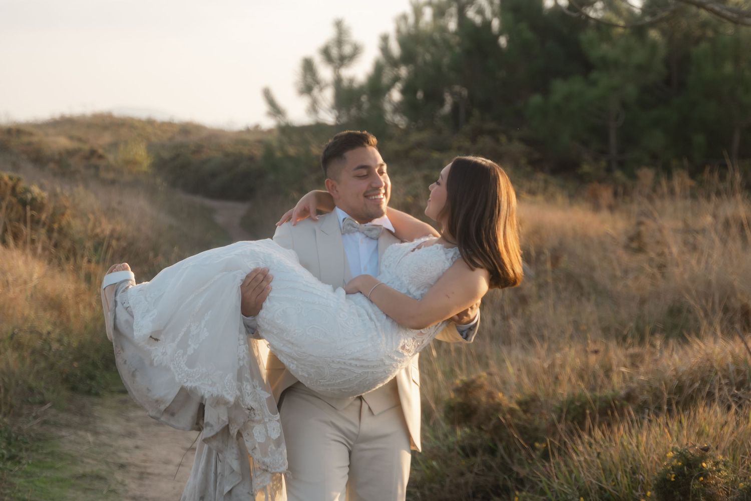 A couple in wedding attire share a romantic moment on a dirt path during golden hour.