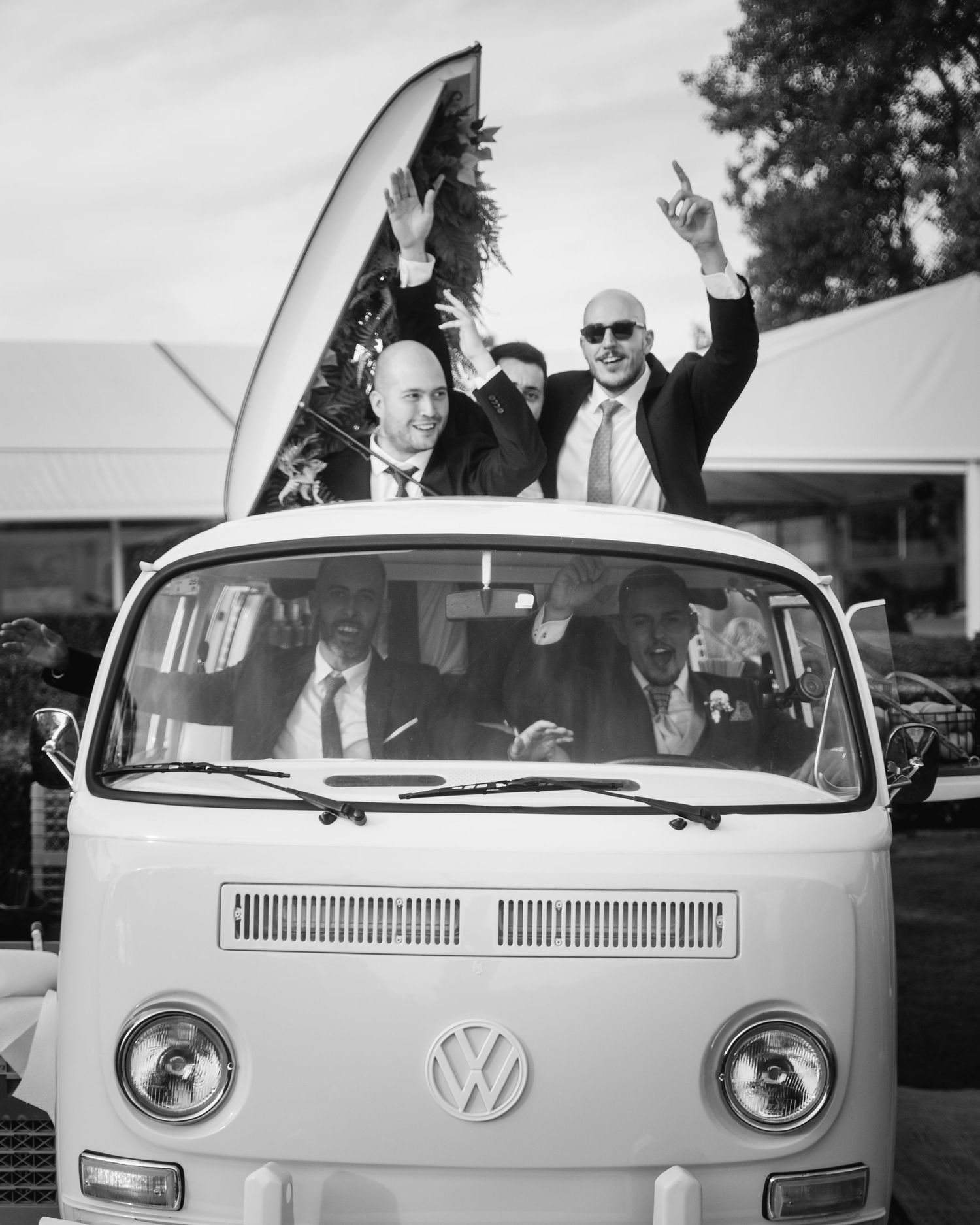 Classic white Volkswagen van with passengers celebrating through the windows.
