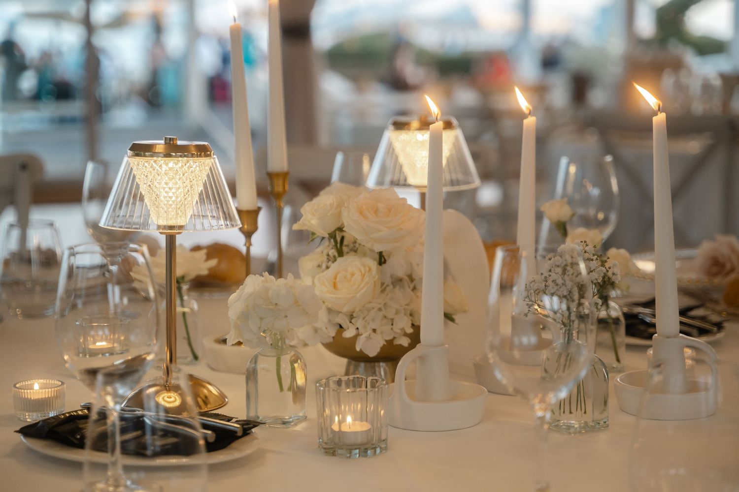 Elegant table settings with white candles and glassware create a romantic atmosphere at a formal dining event.