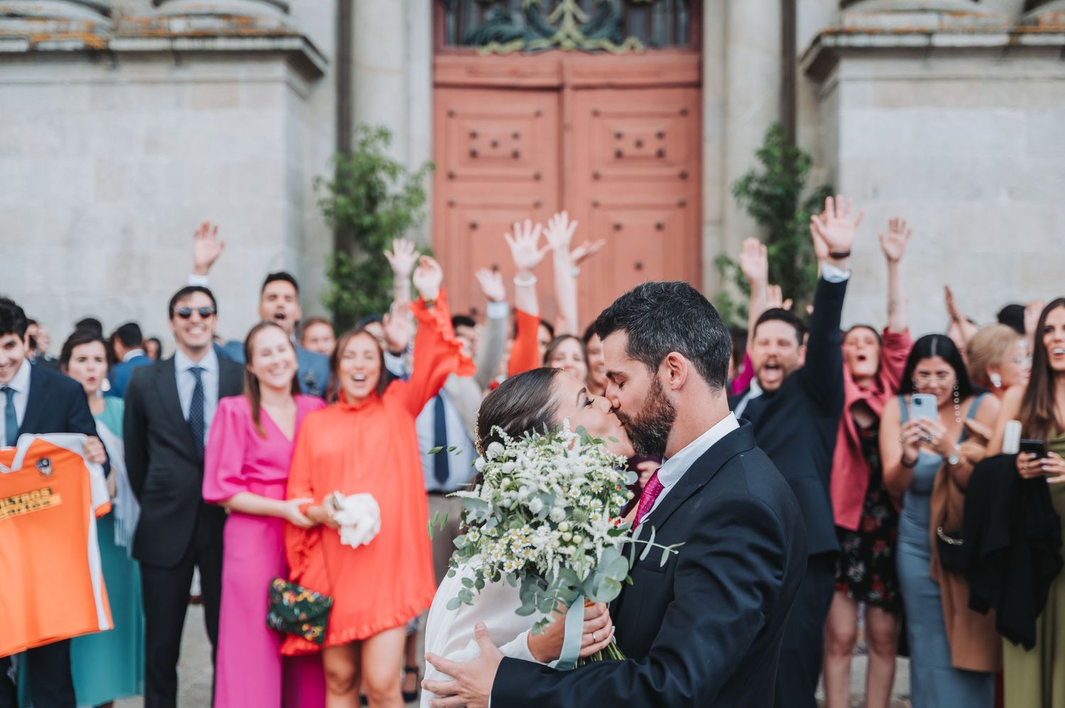 Wedding celebration with guests in colorful attire gathered outside a historic building entrance.