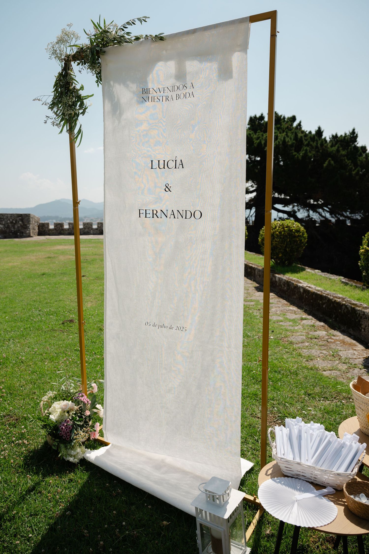 White fabric wedding backdrop with names and wooden posts stands in a grassy outdoor setting.