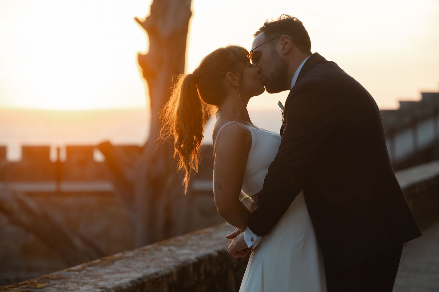 Silhouetted couple embraces during golden sunset with lens flare creating a romantic outdoor atmosphere.