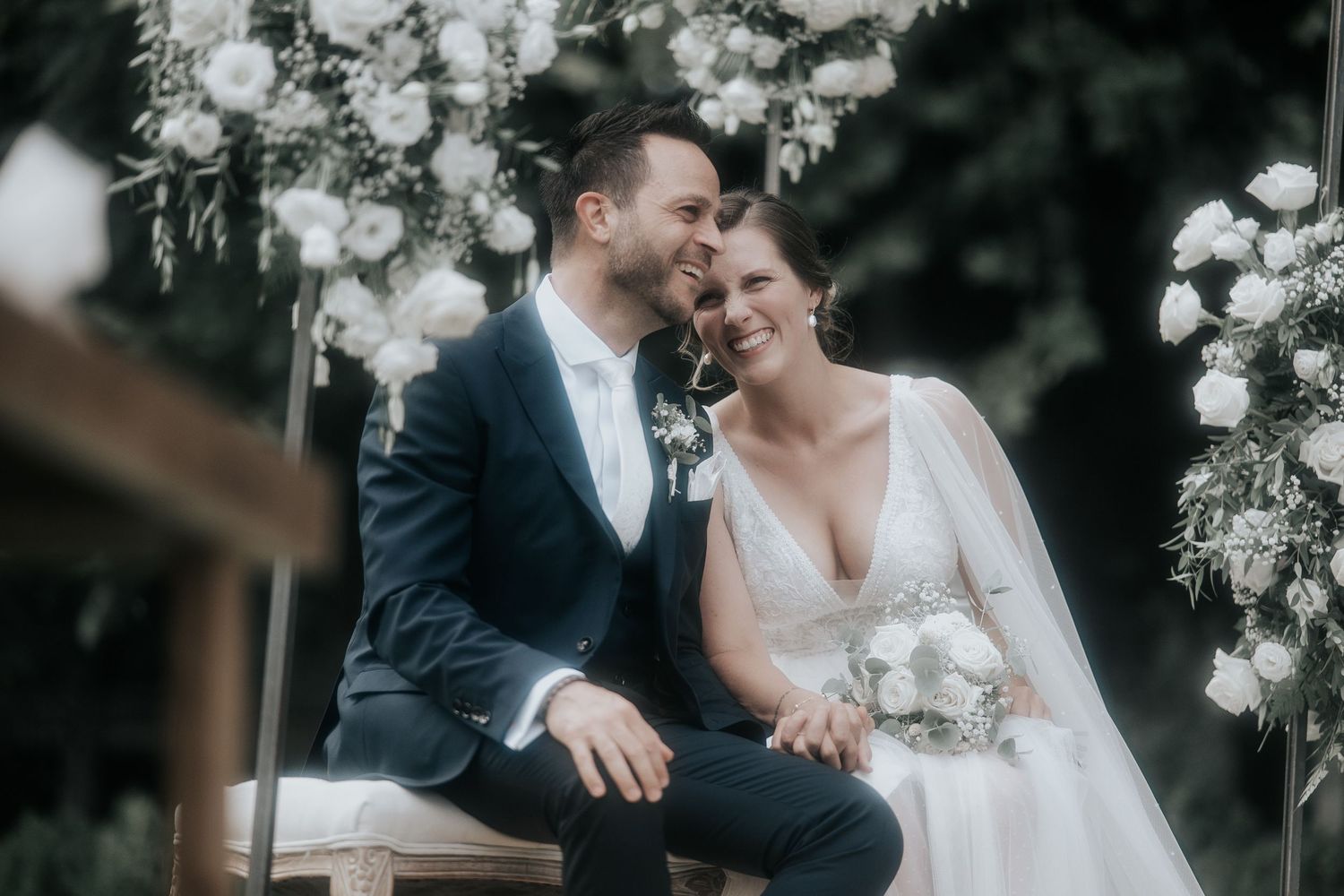 Romantic wedding couple shares intimate moments among white floral decorations outdoors.