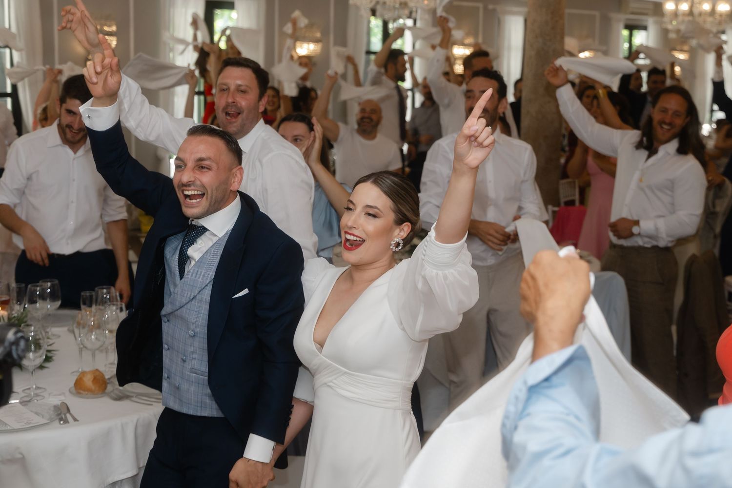 Wedding reception guests dance and celebrate joyfully in an elegant indoor venue with white decor.