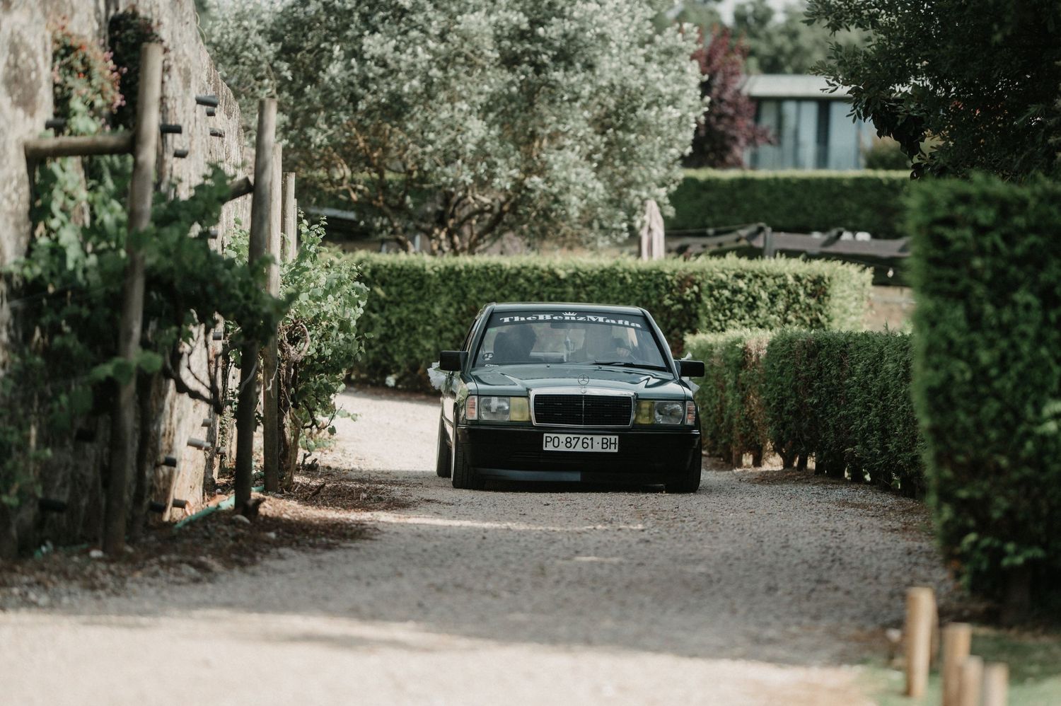 A narrow gravel path leads through a lush garden with trees and shrubs on both sides.