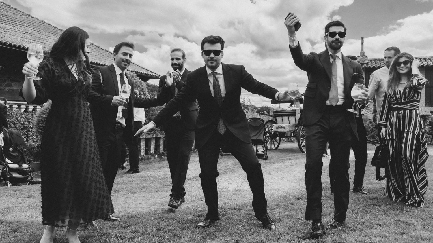 A wedding party poses together in black and white on a sunny day outdoors.