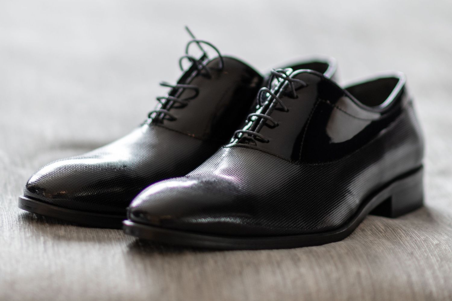 A row of shiny black leather oxford dress shoes arranged at different angles on a light gray background.