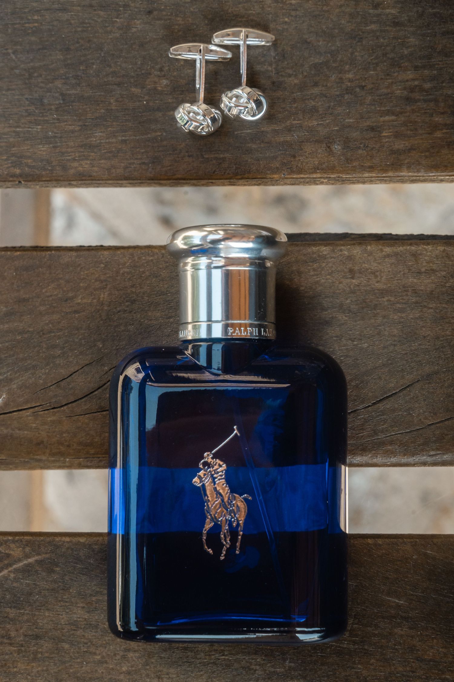Blue glass Ralph Lauren cologne bottle with gold polo player logo displayed on wooden surface.