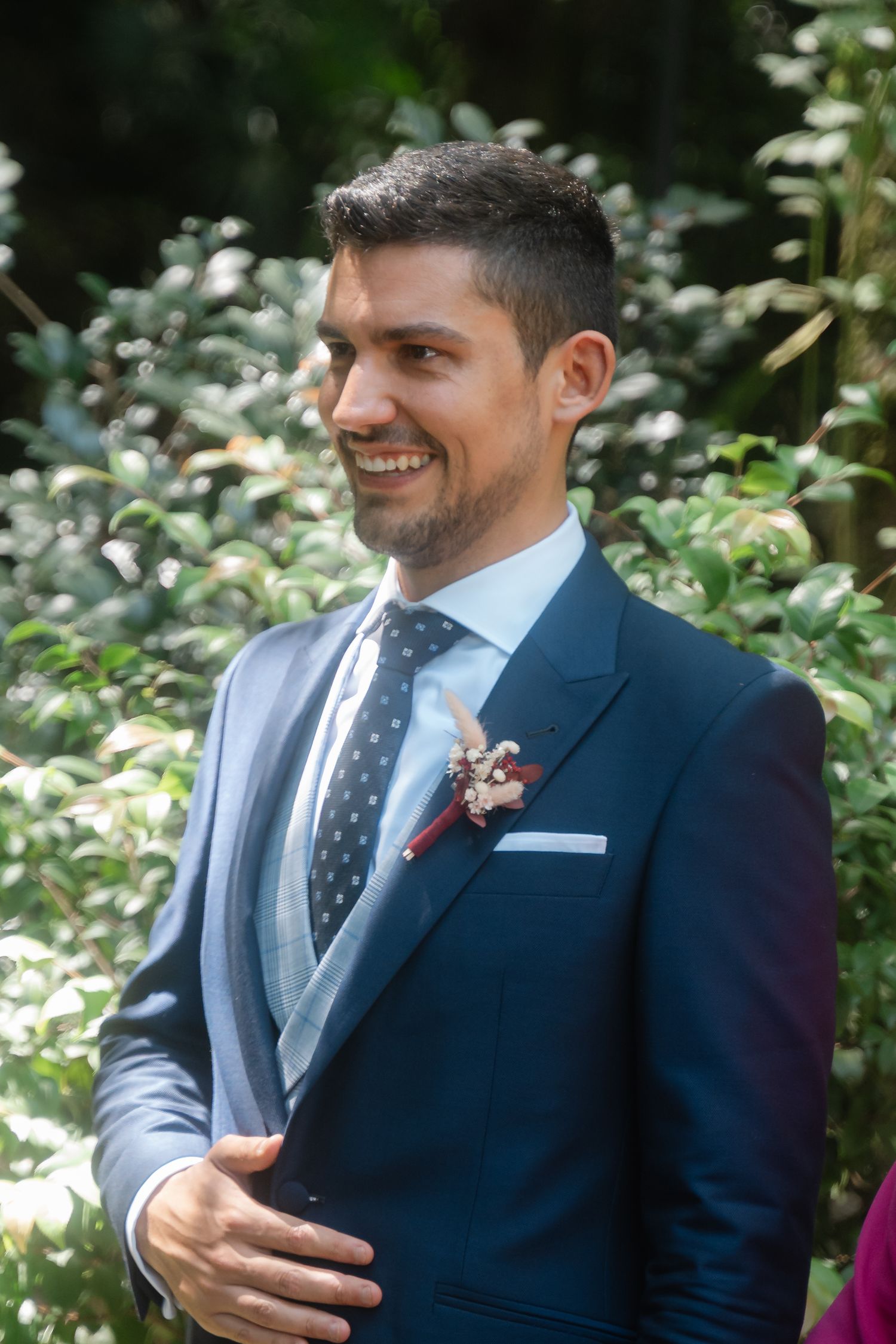 Close-up shots of a groom in a navy suit with polka dot tie smiling during an outdoor wedding ceremony.