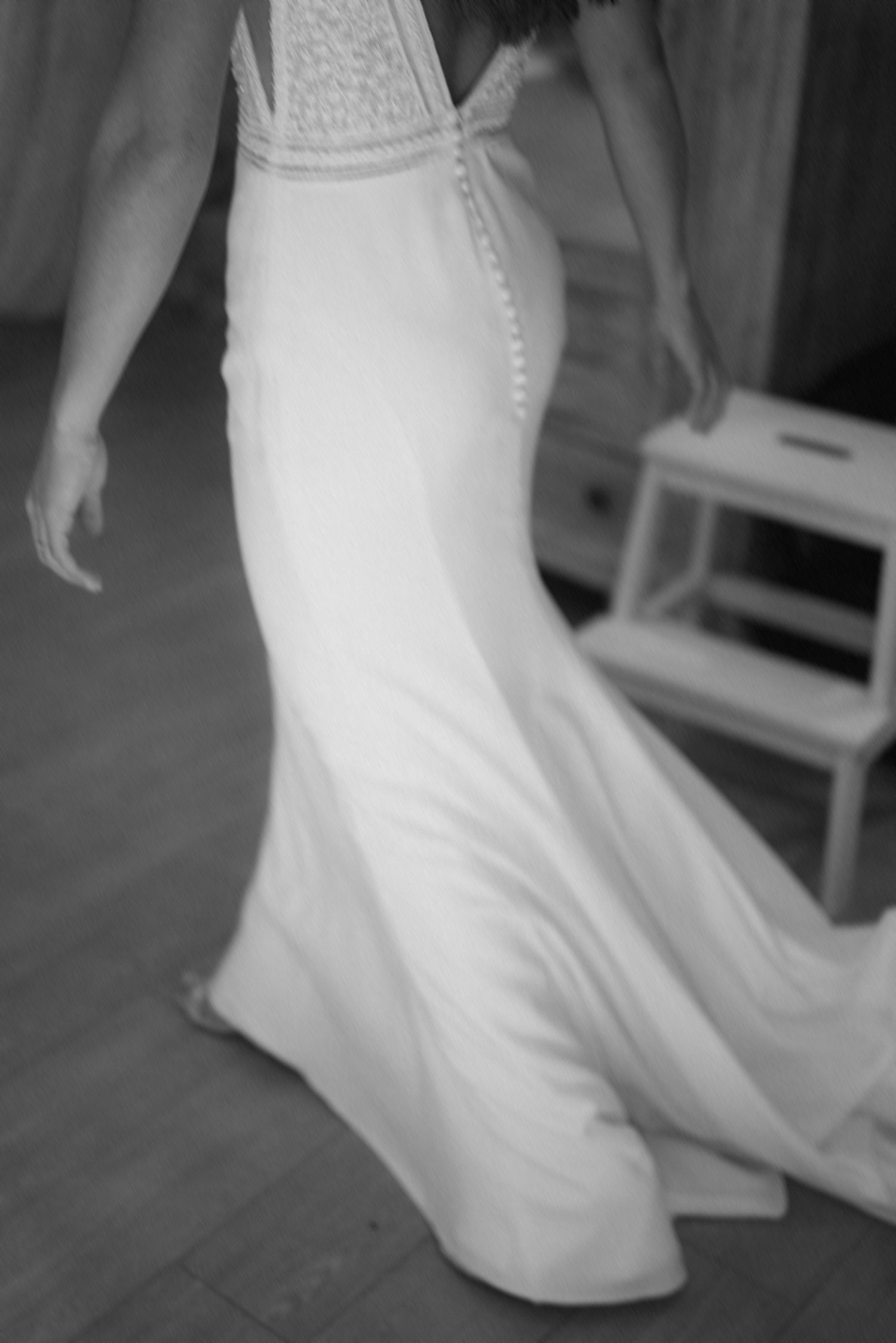 Close-up black and white photo of elegant wedding dress with button details and flowing skirt.