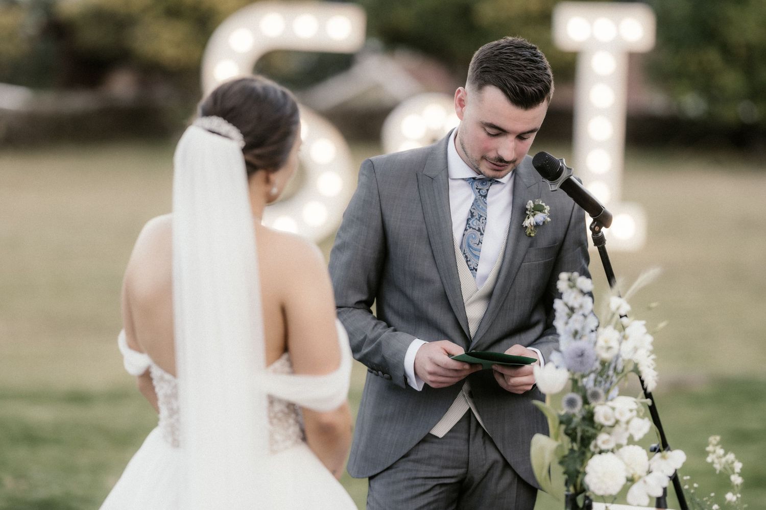 Couple shares intimate moment during wedding ceremony while guests look on in outdoor setting.