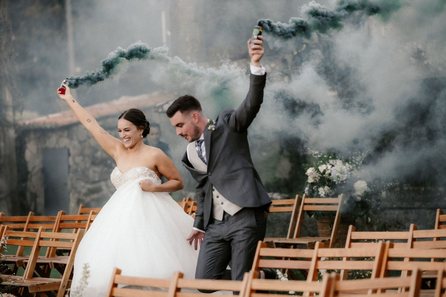 Newlyweds celebrate joyfully with smoke bombs creating dramatic atmospheric effects in the background.