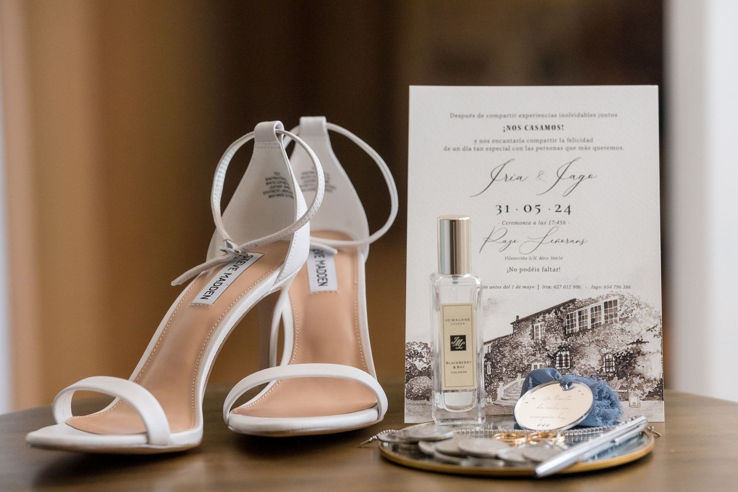 White bridal heels displayed with wedding invitation, perfume bottle and seashell decor against neutral background.