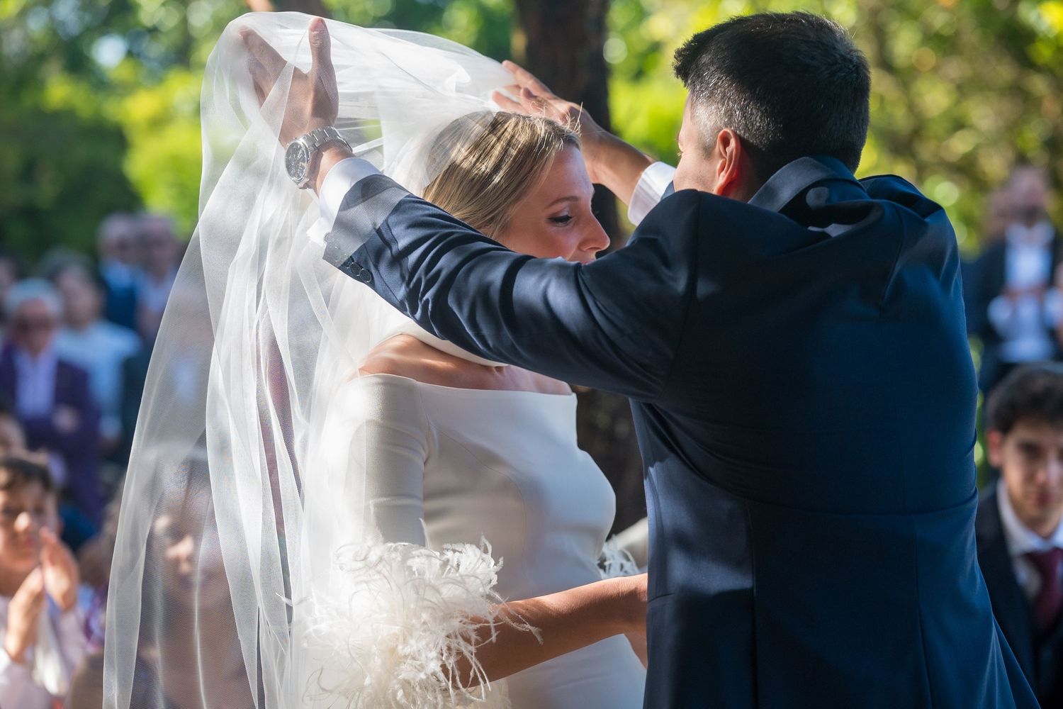 Wedding couple embracing during their first dance with soft natural lighting and guests in background.