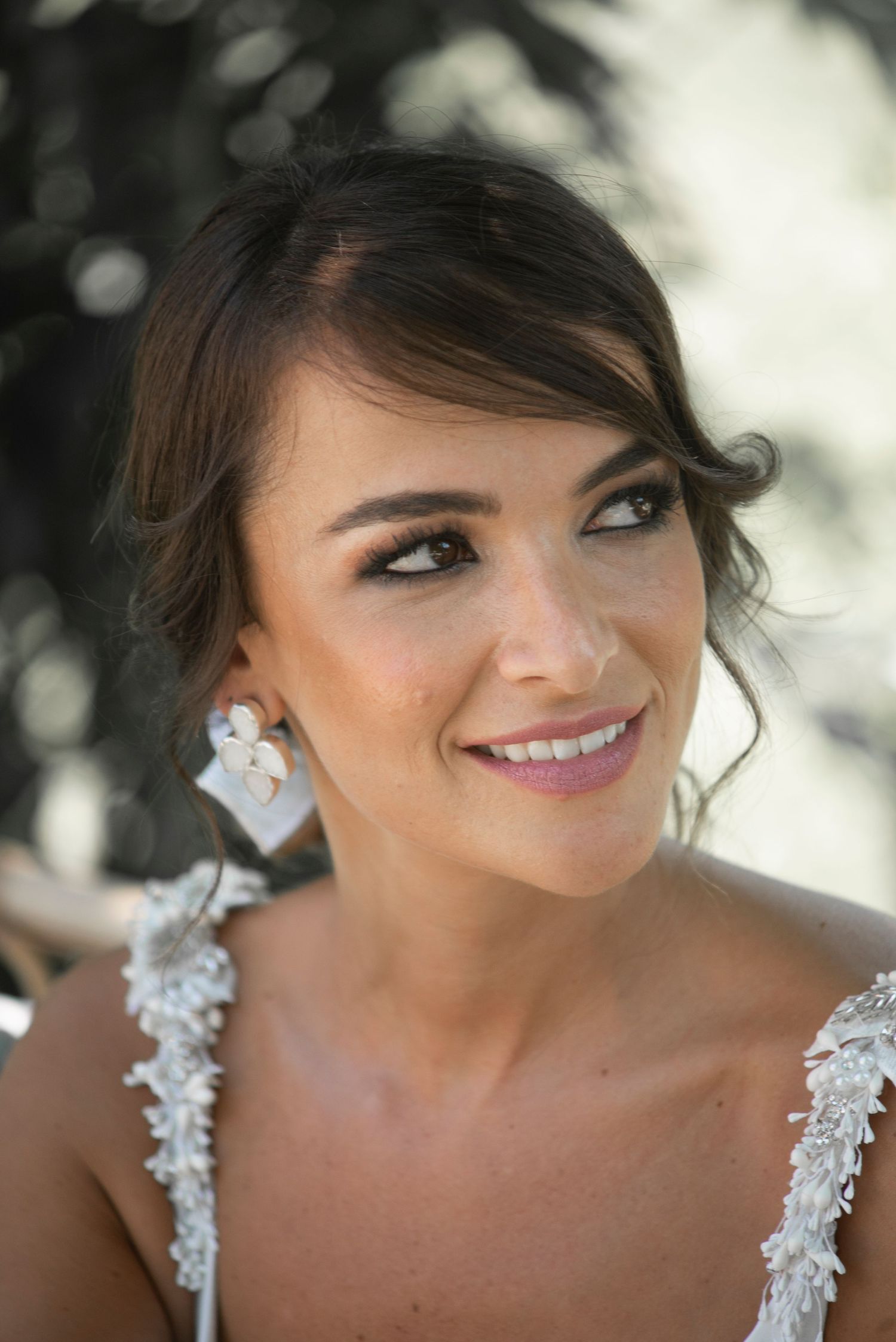 Close-up portrait of bride wearing delicate lace wedding dress and sparkling earrings.