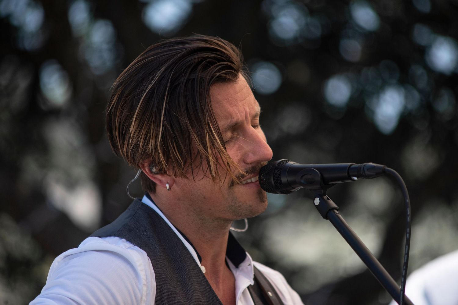 A performer sings passionately into a microphone during an outdoor performance.