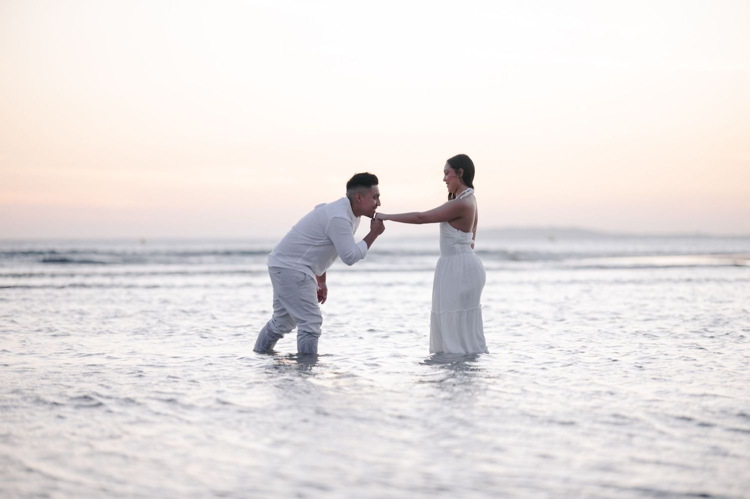 Couple wading in ocean water during golden hour sunset.