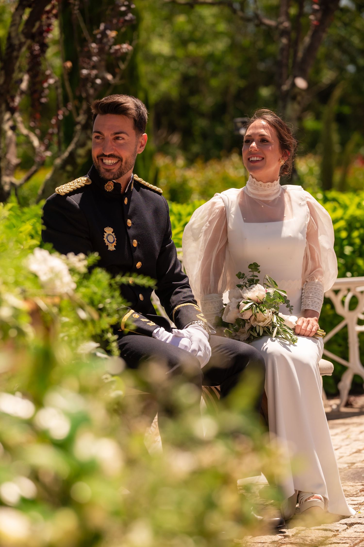 A couple sits together on stone steps in a garden setting during an outdoor wedding celebration.