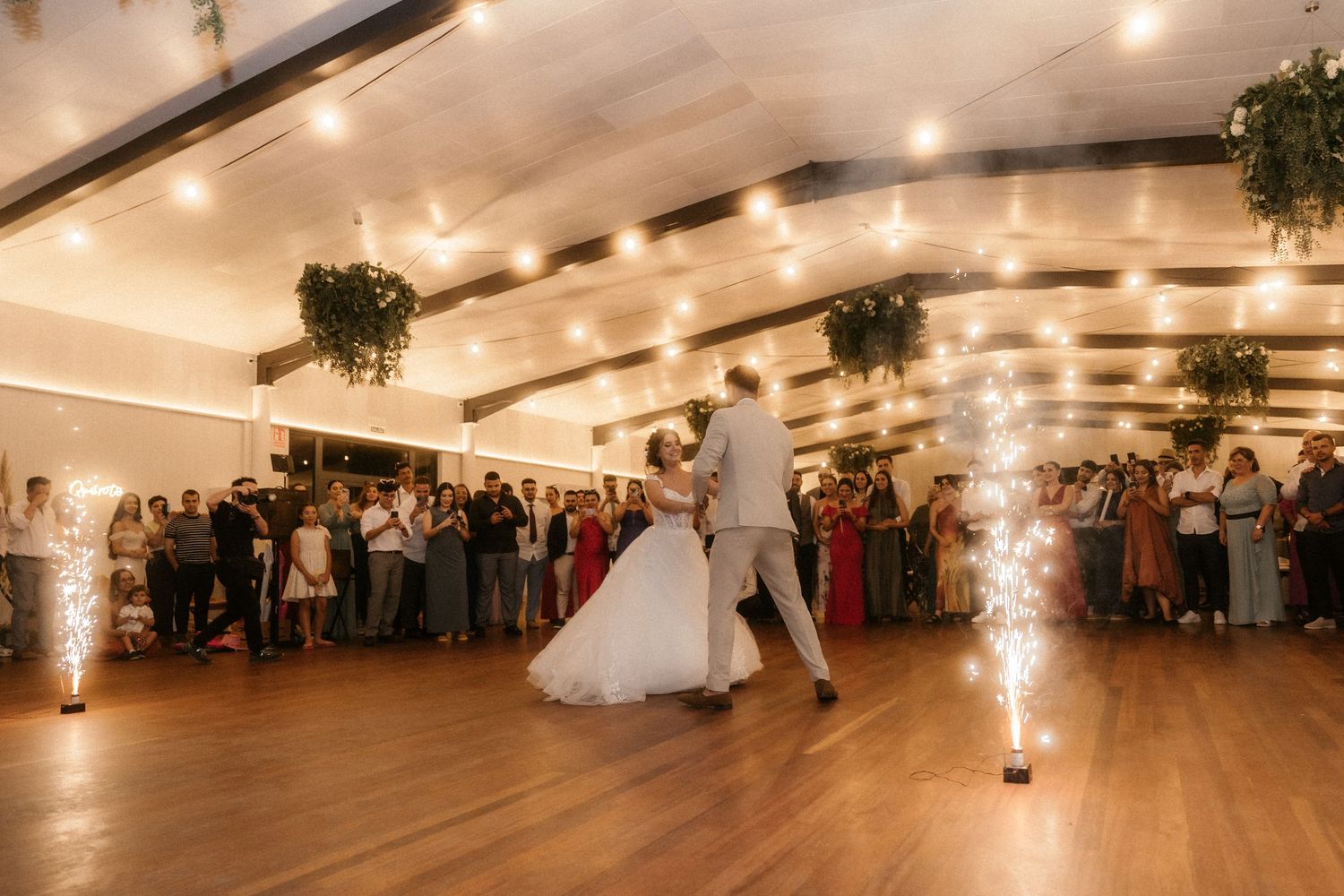 A panoramic view of an elegant wedding reception venue with warm lighting and decorative greenery along the ceiling.
